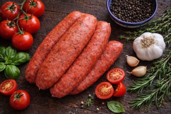 A tomato sausage on a slate background surrounded by fresh tomatoes, garlic & spices
